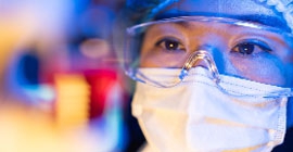 A researcher wearing safety goggles and a mask inspects her work.